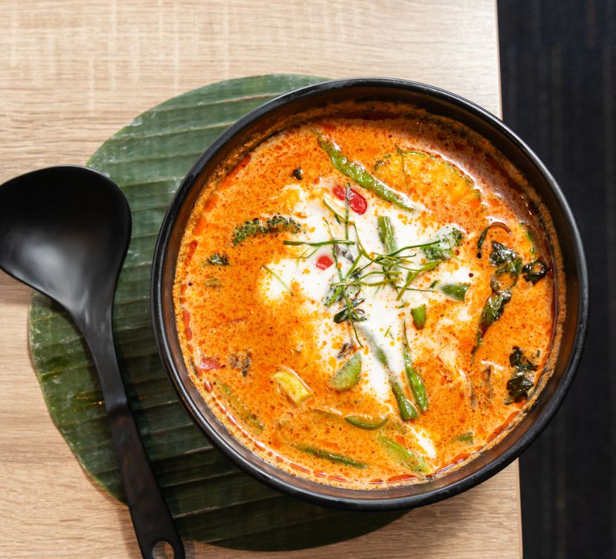 Bowl of Thai panang curry with coconut milk, green beans, kaffir lime leaves, and red chili oil, served in a black bowl